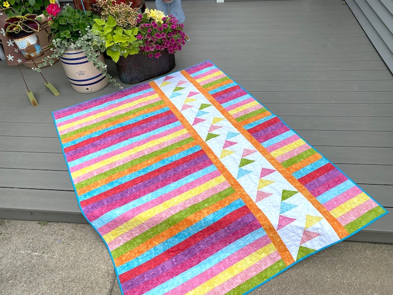 May include: A colorful striped quilt with a white border and a pattern of green, yellow, and blue triangles along one edge.