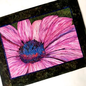 May include: A close-up of a pink flower with a blue and purple centre. The flower is framed by a dark green border.