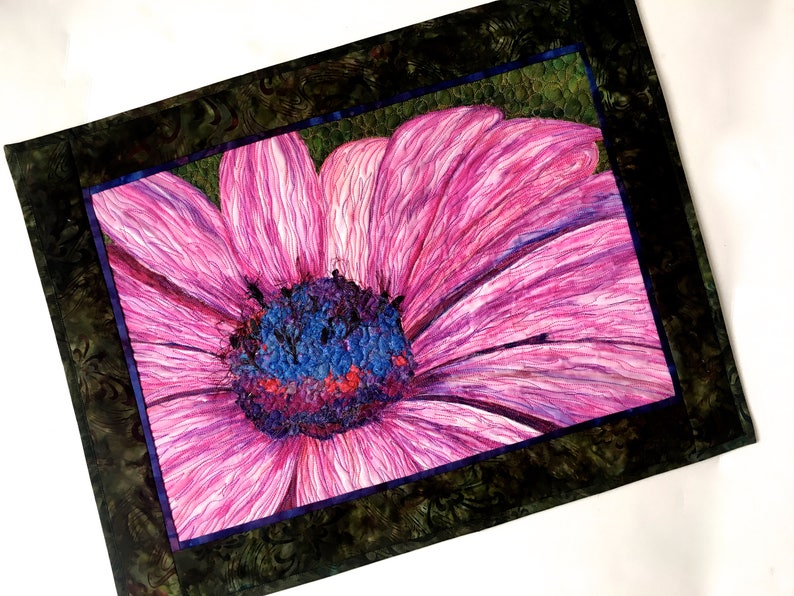 May include: A close-up of a pink flower with a blue and purple centre. The flower is framed by a dark green border.