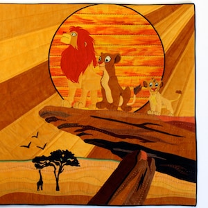 May include: A quilted wall hanging featuring three lions from the movie The Lion King. The lions are standing on a rock formation with a large orange sun behind them. The background is a patchwork of brown and orange fabric.