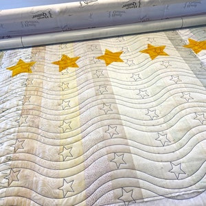 May include: A white quilt with a wavy pattern and five large yellow stars. The quilt is being quilted on a long arm quilting machine.