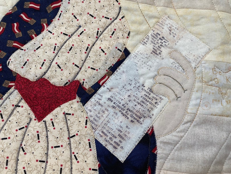 May include: A vintage quilt with a woman's figure in a red and white dress. The quilt is made of various fabrics and includes a piece of paper with French text. The text reads: "De l'Eaudatior stoute que des accords du Greveile aires du personnel exceptionrs venait d'e couveli-nt, a co-alocisat rematrice de L'&eacute;cole du c&ocirc;t&eacute; d ne balayease Men vare itenst".