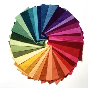 May include: A circular arrangement of colorful paper sheets, fanned out to display a spectrum of hues. The colors range from deep greens and blues to vibrant reds and purples, creating a visually appealing display of color variations.