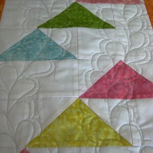 May include: A quilt with a white background and a pattern of triangles in various colors, including yellow, green, blue, pink, and red. The triangles are arranged in a diagonal pattern, and the quilt is quilted with a decorative stitch.