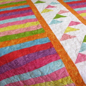 May include: A colorful quilt with a striped pattern on one side and a pattern of triangles on the other side. The quilt is made with bright colors like orange, yellow, green, pink, red, and blue.