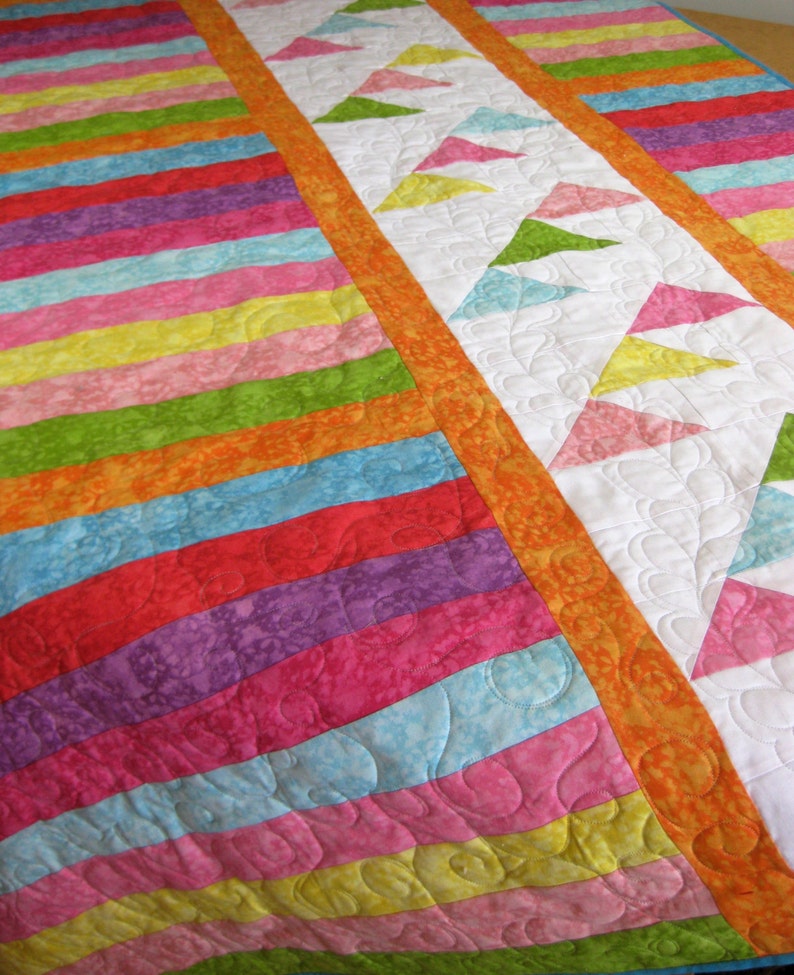 May include: A colorful quilt with a striped pattern on one side and a pattern of triangles on the other side. The quilt is made with bright colors like orange, yellow, green, pink, red, and blue.