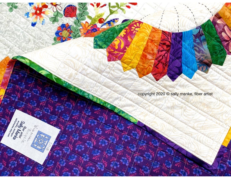 Puede incluir: Una colcha blanca con un dise&ntilde;o de abanico de colores arco&iacute;ris en el centro. La colcha est&aacute; respaldada con una tela morada con un patr&oacute;n floral. La colcha est&aacute; etiquetada con el texto "WIMSICAL Bicycle" y "Sally Manke fiber artist" y el a&ntilde;o de copyright 2020.