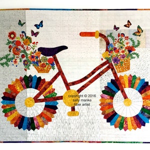 Puede incluir: Una bicicleta roja con una cesta de flores en el manillar. Las ruedas est&aacute;n hechas de tela colorida y la bicicleta est&aacute; sobre un fondo blanco. El texto "copyright &copy; 2016 sally manke fiber artist" est&aacute; impreso debajo de la bicicleta.