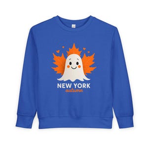 Puede incluir: Sudadera azul con un diseño de fantasma blanco sonriente, rodeado de hojas de arce naranjas y pequeños corazones. El texto "NEW YORK autumn" está impreso debajo. Un diseño de otoño de temporada.