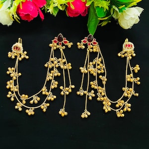 Op de afbeelding: Goudkleurige oorbellen met rode edelsteenaccenten en hangende kettingen van kleine, ronde kralen. De oorbellen hebben een bloemmotief aan de bovenkant en staan tegen een zwarte achtergrond. Sieraden voor speciale gelegenheden.