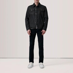 May include: A dark denim jacket with button closures and two chest pockets. The jacket is paired with black jeans and white sneakers. The outfit is a classic, casual style.