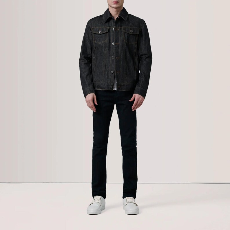 May include: A dark denim jacket with button closures and two chest pockets. The jacket is paired with black jeans and white sneakers. The outfit is a classic, casual style.