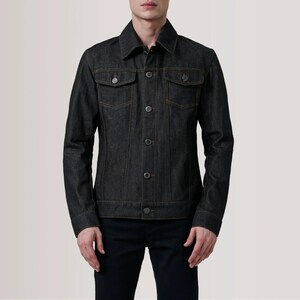 May include: A dark wash denim jacket with a classic collar, two chest pockets, and button closures. The jacket features orange stitching and is worn with black pants. A timeless piece of outerwear.