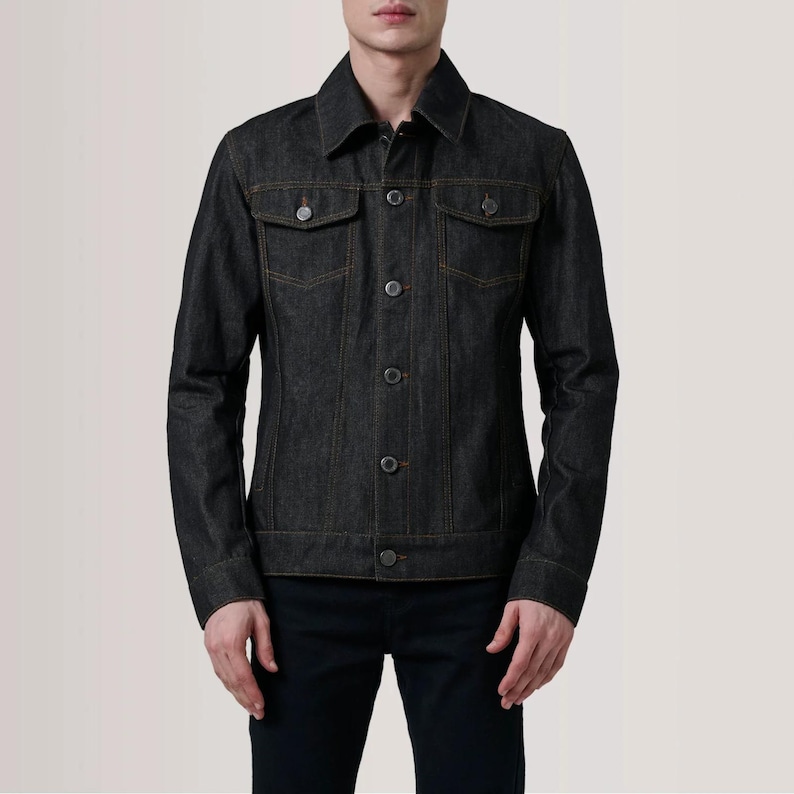 May include: A dark wash denim jacket with a classic collar, two chest pockets, and button closures. The jacket features orange stitching and is worn with black pants. A timeless piece of outerwear.
