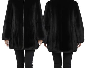 May include: A black, knee-length coat with a high collar and a silver zipper down the front. The coat has long sleeves and a slightly flared shape. The image shows both the front and back of the coat, showcasing its design and fit. The coat is made of a soft, textured material.