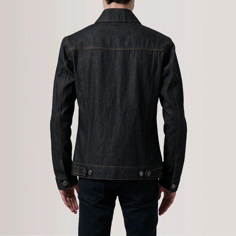 May include: Dark wash denim jacket with a classic collar, button closures, and two chest pockets. The jacket features a tailored fit and is made of durable denim fabric. The stitching is a contrasting tan color.