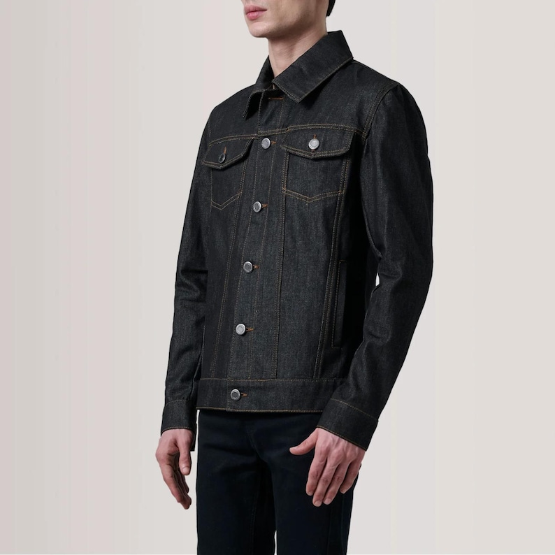 May include: Dark wash denim jacket with orange stitching and silver buttons. The jacket has two chest pockets and a classic collar. The sleeves are long and buttoned at the cuffs. A stylish and versatile outerwear piece.