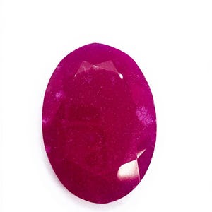 Könnte beinhalten: Ein facettierter, oval geformter Rubin-Edelstein. Der Edelstein hat eine tiefe, satte magenta Farbe mit polierter Oberfläche. Der Edelstein ist vor einem schlichten weißen Hintergrund platziert.