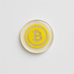 Può includere: Un simbolo Bitcoin giallo su una base circolare trasparente. Il logo Bitcoin, una lettera "B" stilizzata, è centrato all'interno di un cerchio giallo. La base trasparente ha una tonalità leggermente biancastra, su sfondo bianco.