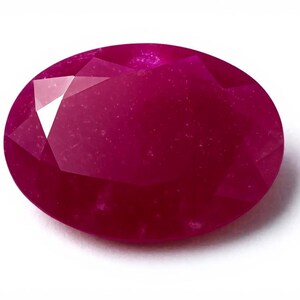 Peut inclure: Une pierre précieuse de rubis de coupe ovale, présentant une teinte rouge profond. La gemme possède de multiples facettes qui reflètent la lumière, créant un aspect brillant. Le rubis est posé sur un fond blanc.