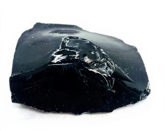 May include: A large, irregularly shaped piece of obsidian. The natural volcanic glass has a deep black color with a glossy, reflective surface. The edges are rough and jagged, showing the stone's fractured nature.