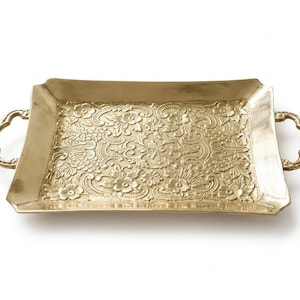 May include: A rectangular gold-coloured metal tray featuring an intricate embossed floral pattern across its surface. The tray includes two decorative curved handles on opposite sides, with a smooth, raised border framing the detailed centre design.