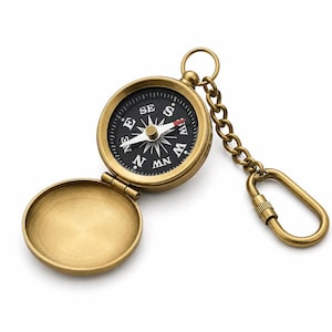 May include: A brass-toned metal pocket compass keyring with an open hinged lid. The compass features a black circular face with white cardinal direction markings and a needle with a red tip, attached to a chain and a screw-lock carabiner clip.