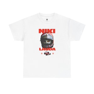 Könnte beinhalten: Weißes T-Shirt mit einer Grafik eines Rennhelms und dem Namen "NIKI LAUDA" in roten Blockbuchstaben. Unter dem Namen befindet sich eine kleine rote Rennwagengrafik. Der Helm hat ein rot-weiß-blaues Design.