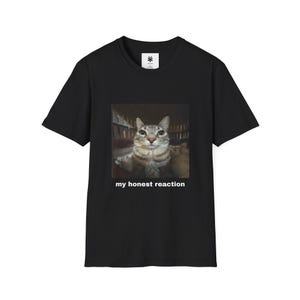 May include: Black t-shirt featuring a cat image with the text "my honest reaction." The cat is gray and white, with a surprised expression. The shirt has a crew neck and short sleeves.