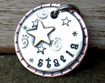 May include: A silver and copper dog tag with a star design and the word "starla" engraved on it.