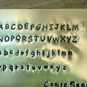 以下が含まれることがあります： 金属製のプレートに、大文字と小文字のアルファベットと「Comic Sans」という文字が刻まれています。