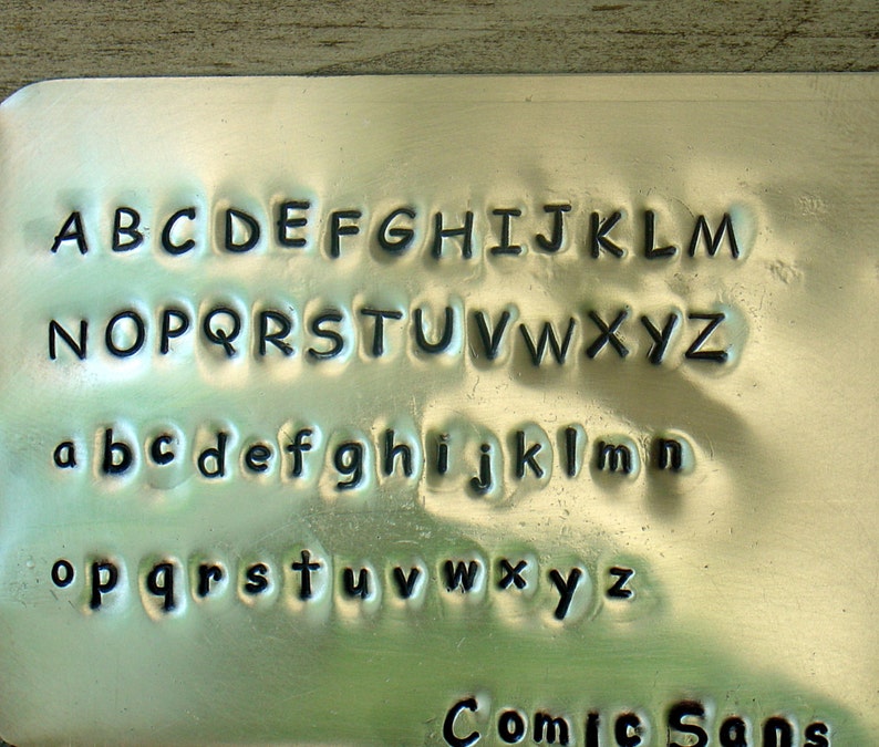 以下が含まれることがあります： 金属製のプレートに、大文字と小文字のアルファベットと「Comic Sans」という文字が刻まれています。