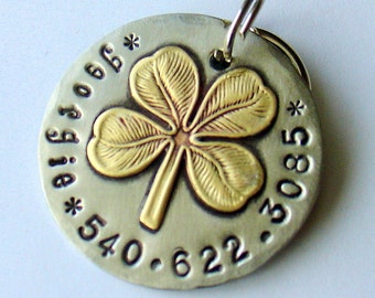 Könnte beinhalten: Ein silbernes Metallschild mit einem vierblättrigen Kleeblatt in Gold und Kupfer. Das Schild trägt die Zahlen 540.622.3085 und den Text "a big job*" eingraviert.