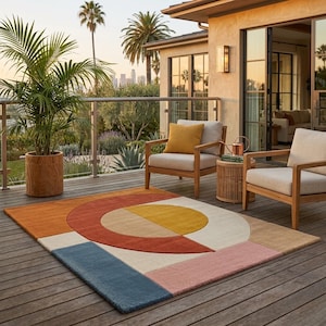 Puede incluir: Una colorida alfombra geométrica con un diseño moderno. La alfombra presenta un semicírculo naranja, un cuarto de círculo amarillo y bloques rectangulares azules, rosas y beige. La alfombra está sobre una terraza de madera con muebles de exterior.