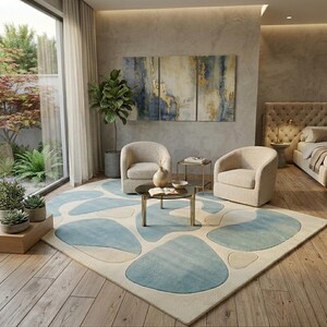 May include: A contemporary living room with a large rug featuring a light blue and cream abstract pattern. Two beige armchairs face a small round coffee table. A triptych painting hangs above the chairs, and a large window is on the left.