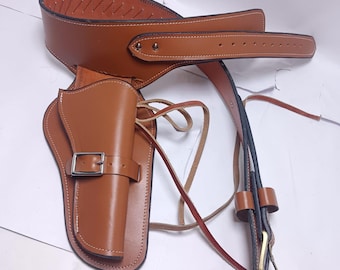 Könnte beinhalten: Ein braunes Leder-Waffenholster- und Gürtel-Set. Das Holster hat einen Schnallenverschluss und ist an einem Gürtel mit einem genähten Design befestigt. Das Set enthält einen Riemen und eine Messingschnalle.