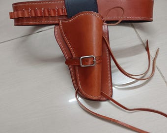 Könnte beinhalten: Ein braunes Leder-Waffenholster- und Gürtel-Set. Das Holster ist für eine Schusswaffe konzipiert und wird mit einer Schnalle befestigt. Der Gürtel hat Schlaufen für Munition. Das Set ist mit weißem Faden genäht.