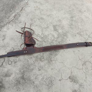 Könnte beinhalten: Ein braunes Leder-Gürtel- und Holster-Set. Der Gürtel hat eine Schnalle und eine Reihe von Patronenschlaufen. Das Holster ist am Gürtel befestigt und hat eine Tasche für eine Pistole. Das Leder ist abgenutzt.