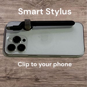 May include: A black Smart Stylus clipped to a smartphone. The stylus has a silver adjustable clip and a black tip. The phone is silver with three camera lenses. Text on the image reads "Smart Stylus" and "Clip to your phone."