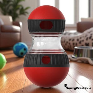 Puede incluir: Un juguete para perros rojo y negro con una sección central transparente. El juguete tiene forma redondeada con aberturas laterales. Otros juguetes para perros son visibles en el fondo.