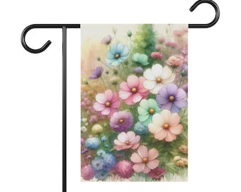 Puede incluir: Una bandera de jardín rectangular que presenta una ilustración estilo acuarela de varias flores cosmos en tonos rosa, azul, morado y blanco, suspendida de un soporte de metal negro con dos ganchos curvos en la parte superior.