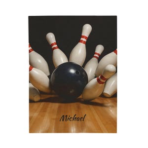 May include: A bowling scene with a black bowling ball striking white bowling pins with red stripes. The pins are arranged around the ball on a wooden lane. The name "Michael" is written in cursive at the bottom.