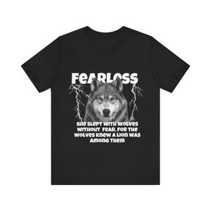 May include: Black t-shirt with a wolf graphic and the word "FEARLESS" in white. The text "SHE SLEPT WITH WOLVES WITHOUT FEAR, FOR THE WOLVES KNEW A LION WAS AMONG THEM" is below the wolf image.