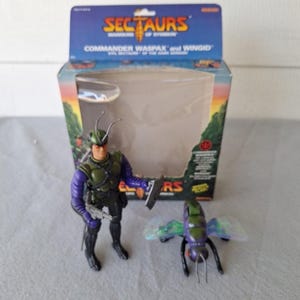 May include: A Sectaurs Commander Waspax action figure with a Wingid insect figure, both in a box. The Commander Waspax figure is green, purple, and black, holding a weapon. The box has the Sectaurs logo and a landscape scene.