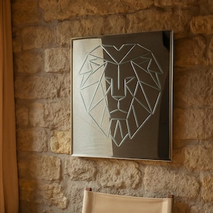 May include: A geometric lion art piece hangs above a wooden chair with a canvas seat. The artwork is framed and features a lion's head composed of angular lines. The chair has a light-colored canvas seat and wooden frame. A small wooden stool is to the left.