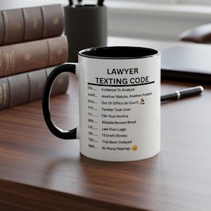 Puede incluir: Taza de cerámica blanca con interior y asa negros. La taza presenta el texto "LAWYER TEXTING CODE" y una lista de abreviaturas con sus significados, como "ETA Evidence To Analyze" y "LOL Law Over Logic".