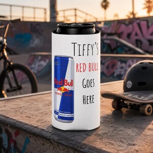 May include: White can cooler with the text "TIFFY'S RED BULL GOES HERE" and a Red Bull energy drink can graphic. The can cooler is designed to keep beverages cold. The background includes a skateboard and a BMX bike.
