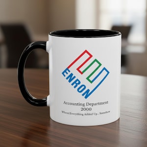 Może przedstawiać: Biały ceramiczny kubek z czarnym wnętrzem i uchwytem. Kubek posiada logo Enron w kolorze czerwonym, zielonym i niebieskim, wraz z tekstem "ENRON" i "Accounting Department 2000". Kubek ma również tekst "Where Everything Added Up... Somehow."