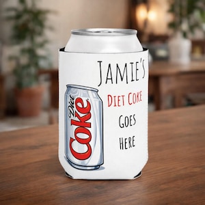 May include: A white drinks can cooler with the text "Jamie's Diet Coke Goes Here." It features a graphic of a Diet Coke can in red, white, and silver. The cooler is designed to hold a standard-sized soft drink can.