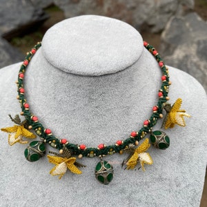 May include: A green and coral beaded necklace with yellow crocheted flowers and green and gold pendant charms.